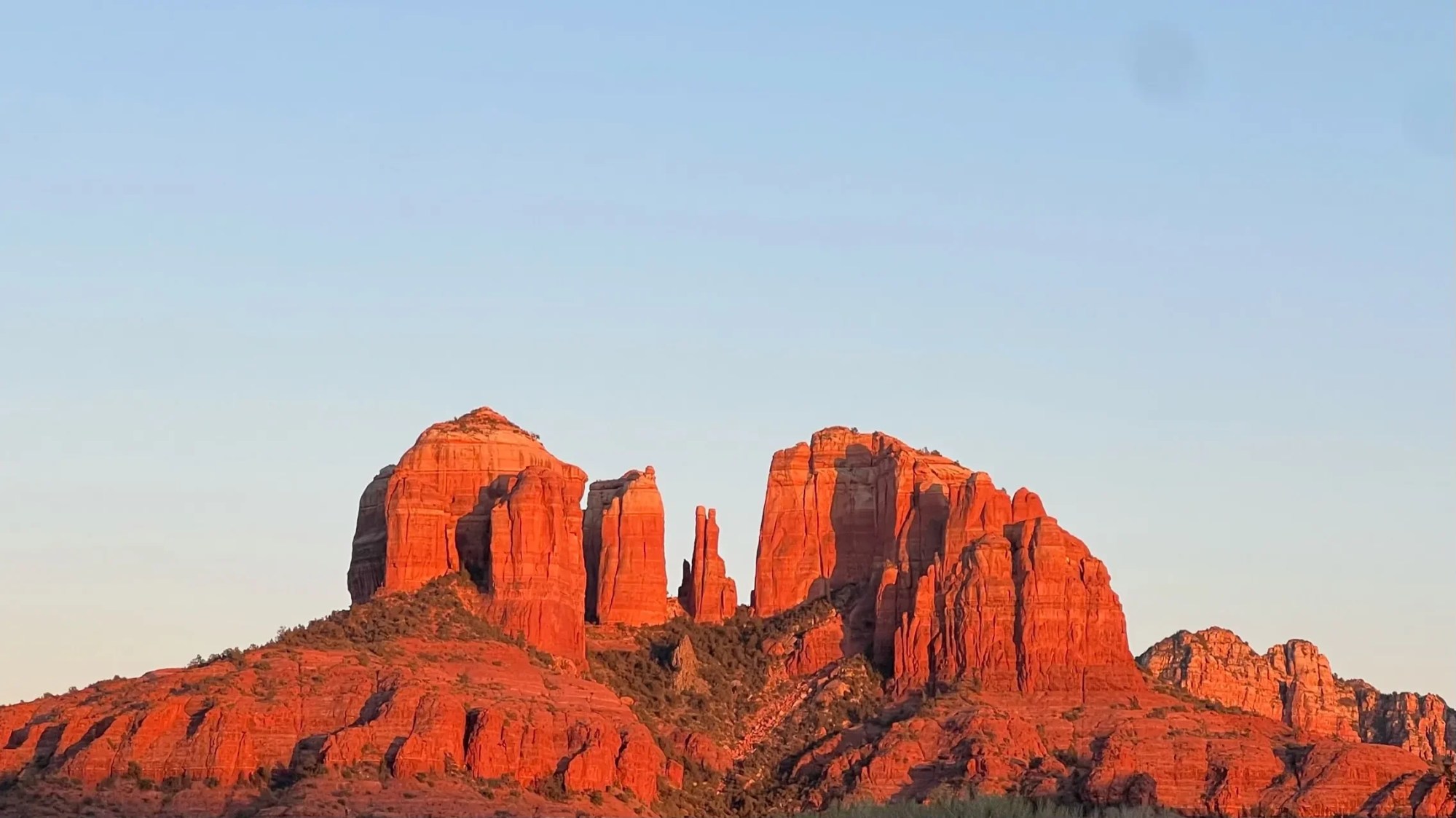 Red rock formations against a clear blue sky, illuminated by sunset.