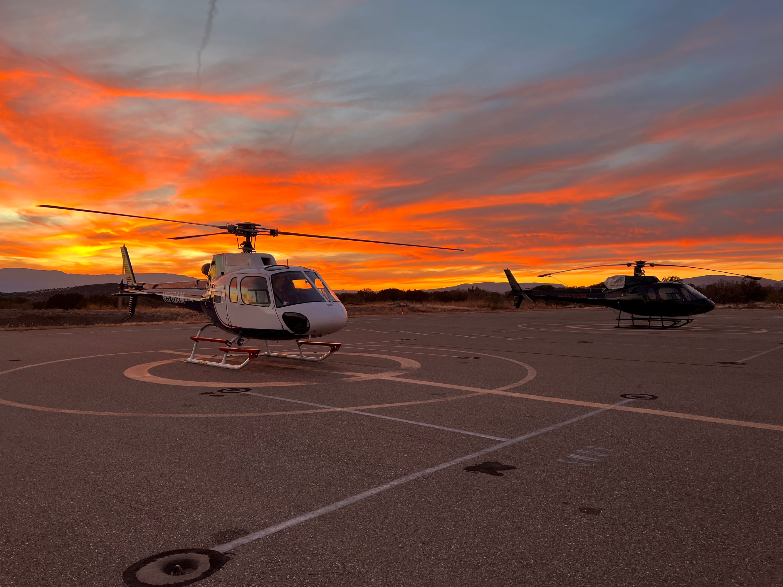 Two helicopters at the sedona airport during sunset , with a vibrant orange sky.