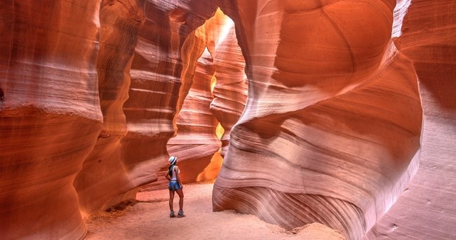 Person standing in narrow, winding sandstone canyon with light filtering through.