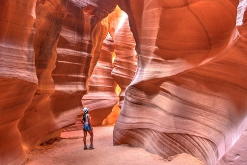 Person standing in narrow, winding sandstone canyon with light filtering through.