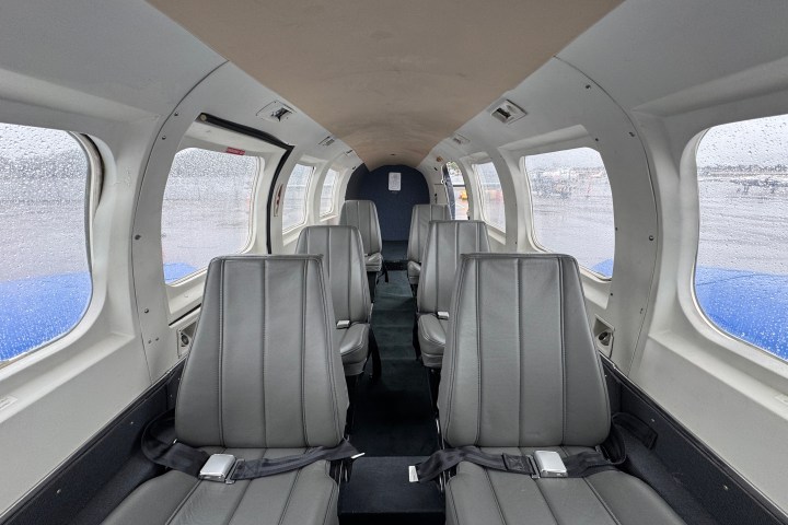 Interior of a small private airplane with six gray leather seats and rain on windows.