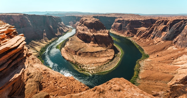 Panoramic view of Horseshoe Bend with river winding around red rock cliffs under clear sky.