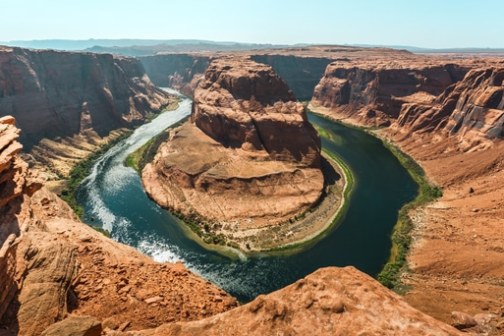 Panoramic view of Horseshoe Bend with river winding around red rock cliffs under clear sky.